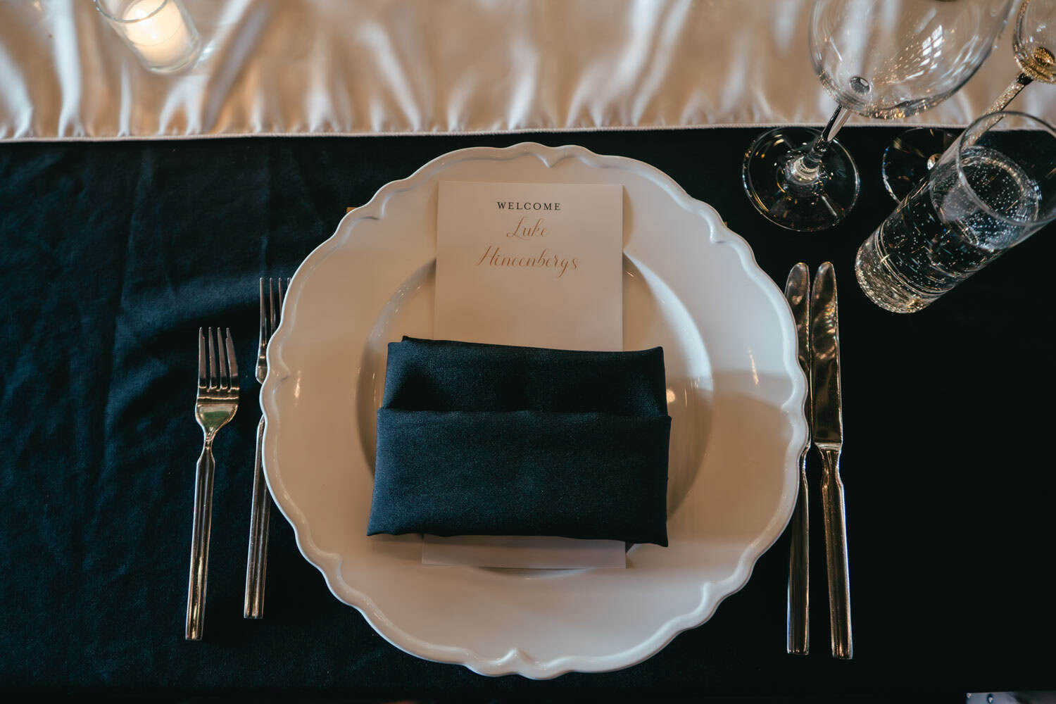 Formal table setting with white plate, black napkin, and glassware.