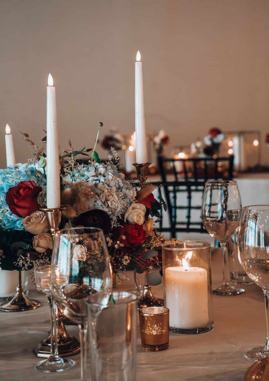 Wedding table setup with candles, flowers, and glassware for elegant event.