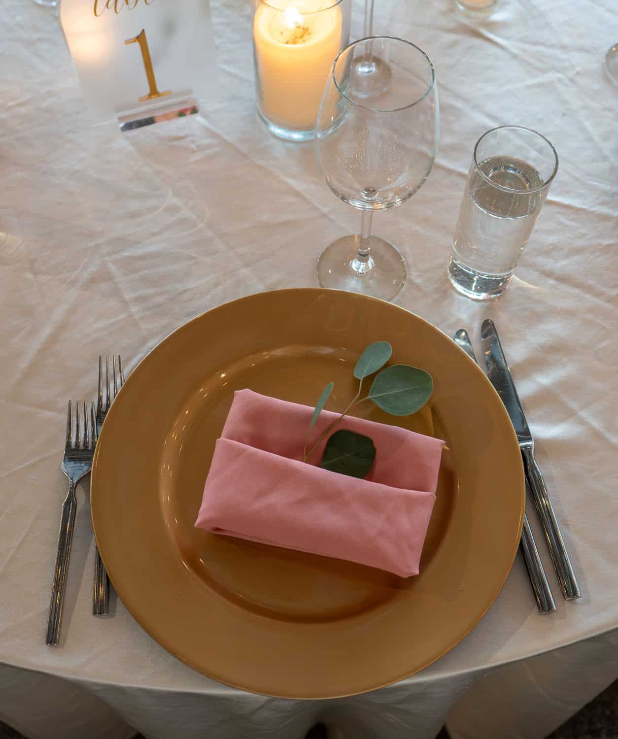 Table setting with pink napkin, glassware, and candles for celebration.
