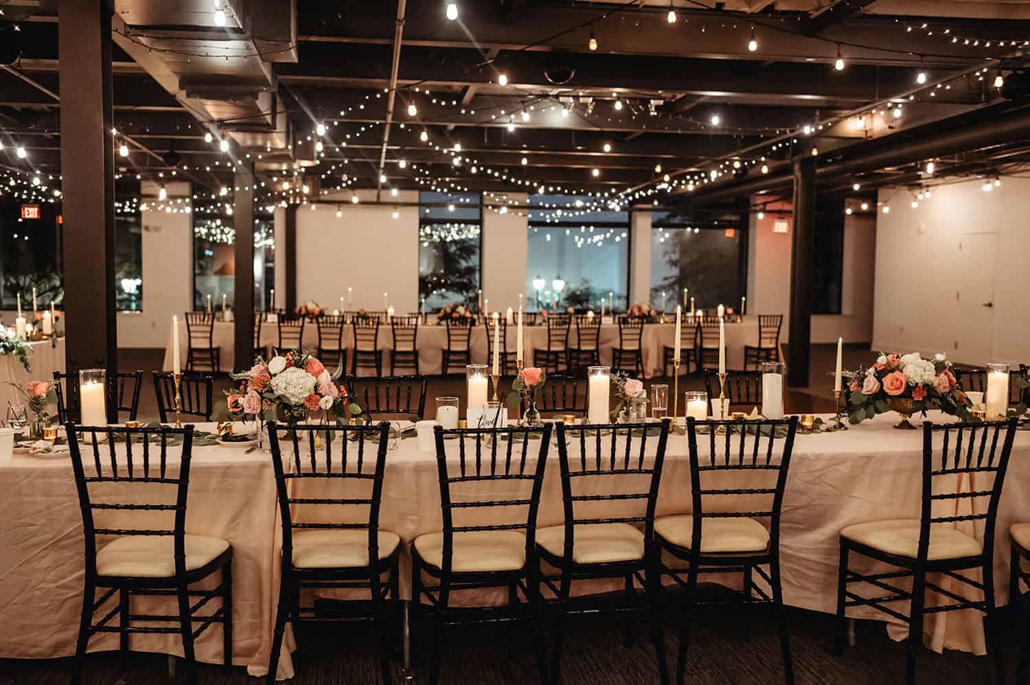 Indoor event space decorated with string lights and floral centerpieces.