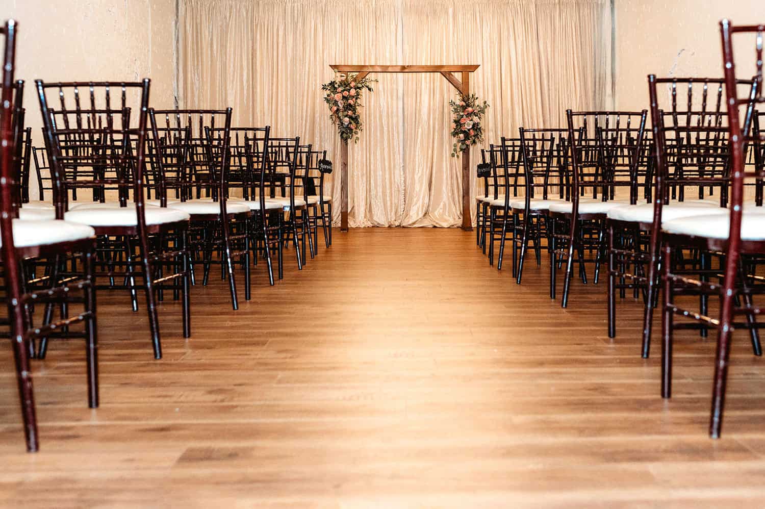 Wedding ceremony setup with chairs and floral arch in a decorated hall.