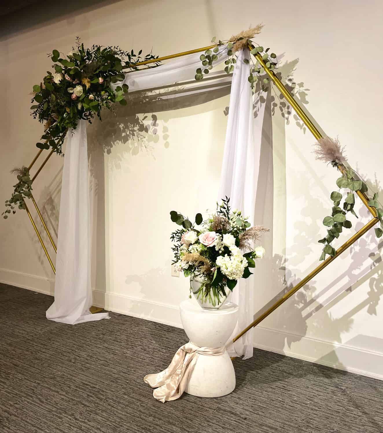 Stylish wedding arch with floral arrangements and white drapes for celebration.