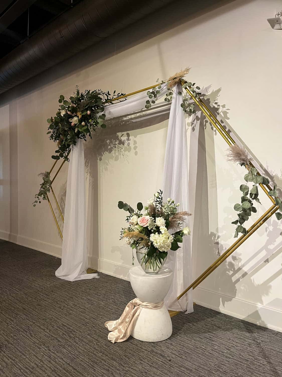 Stylish wedding arch with white drapes and floral arrangements at SKY Armory.