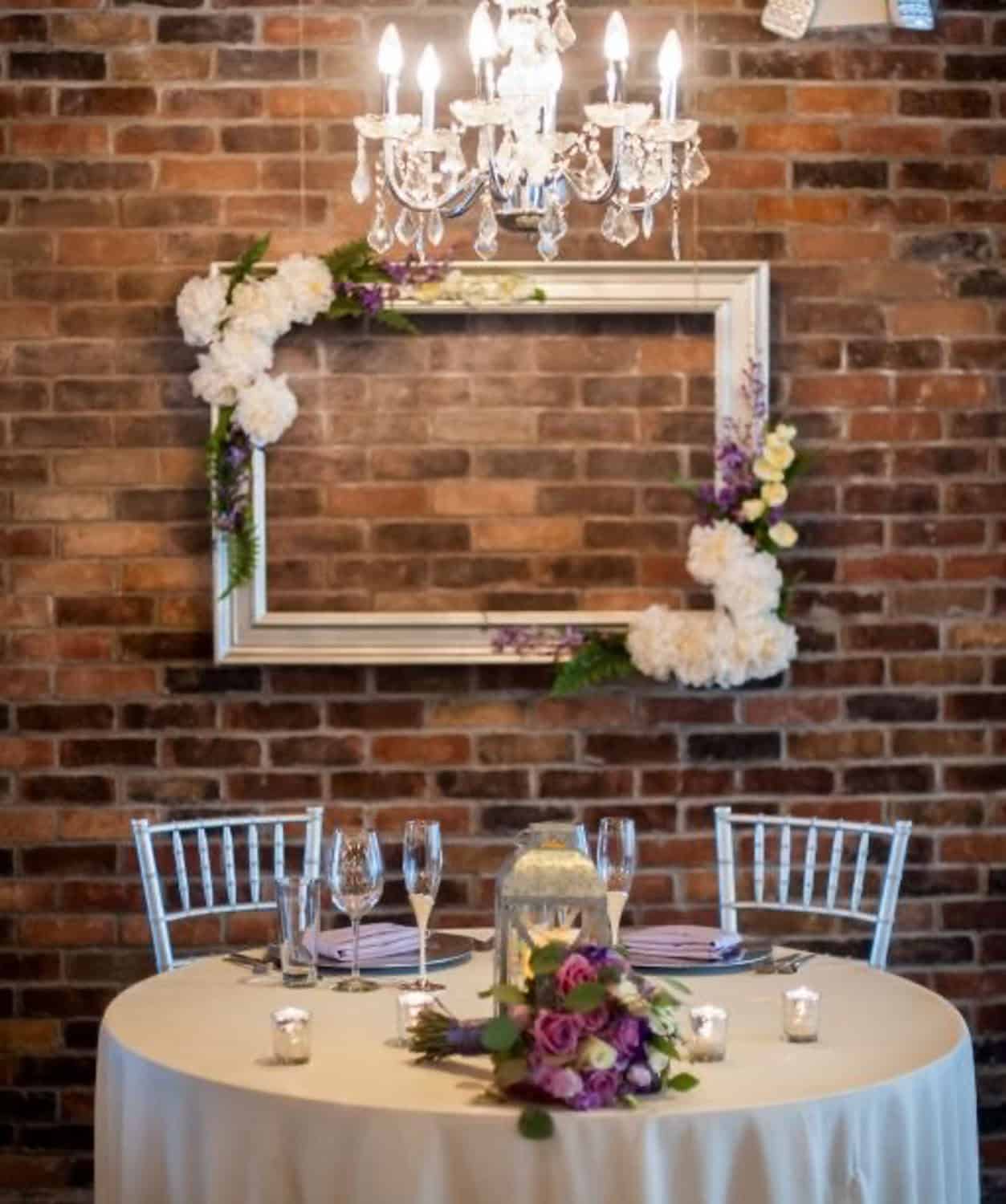 Wedding reception table with floral centerpiece and chandelier backdrop.