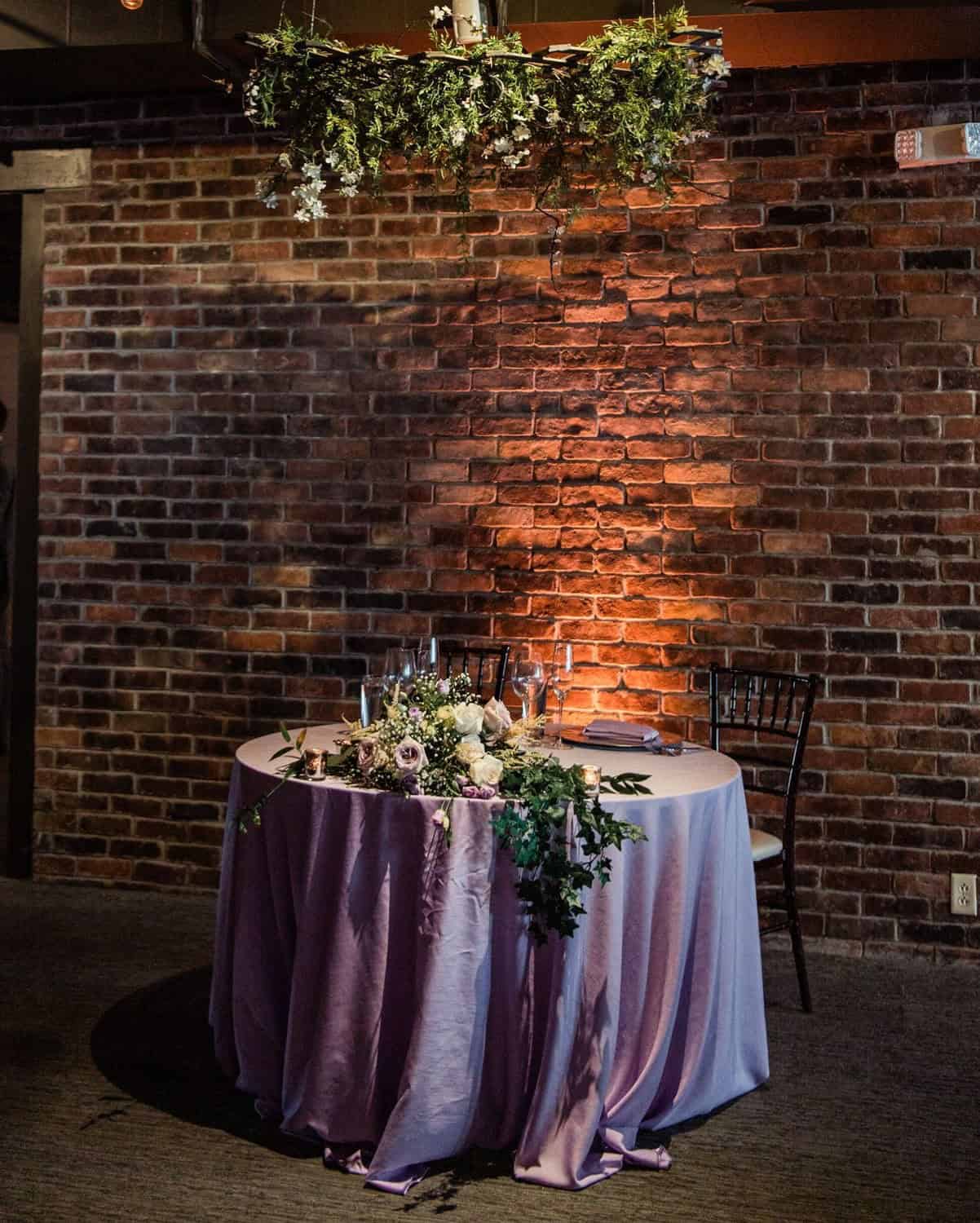 Wedding reception table with floral centerpiece and purple tablecloth.
