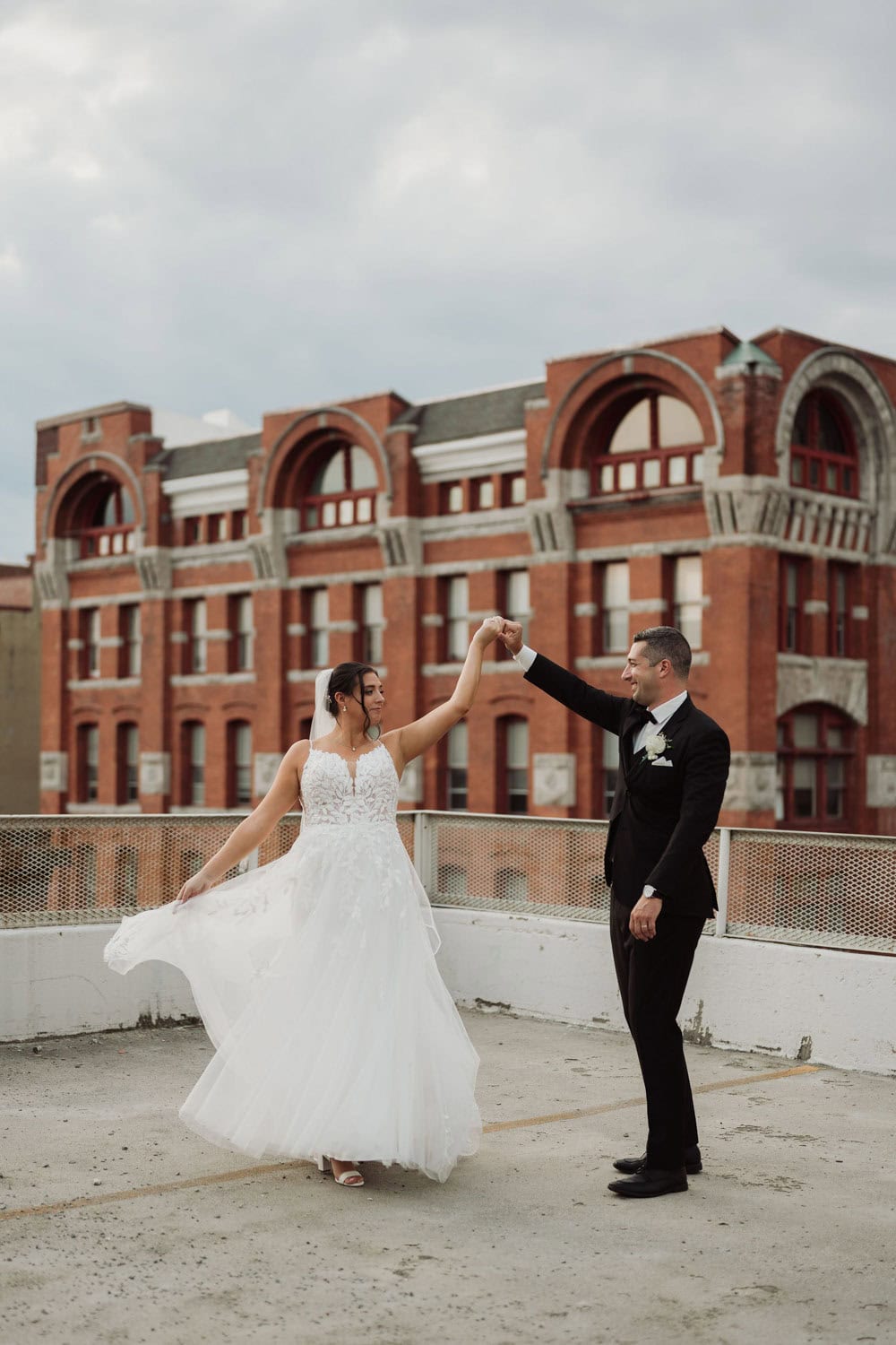 Bride and groom dancing on rooftop with historic building background.