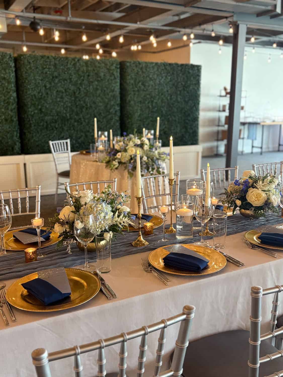 Decorated event table with gold plates, navy napkins, floral centerpieces, and candleholders at SKY.