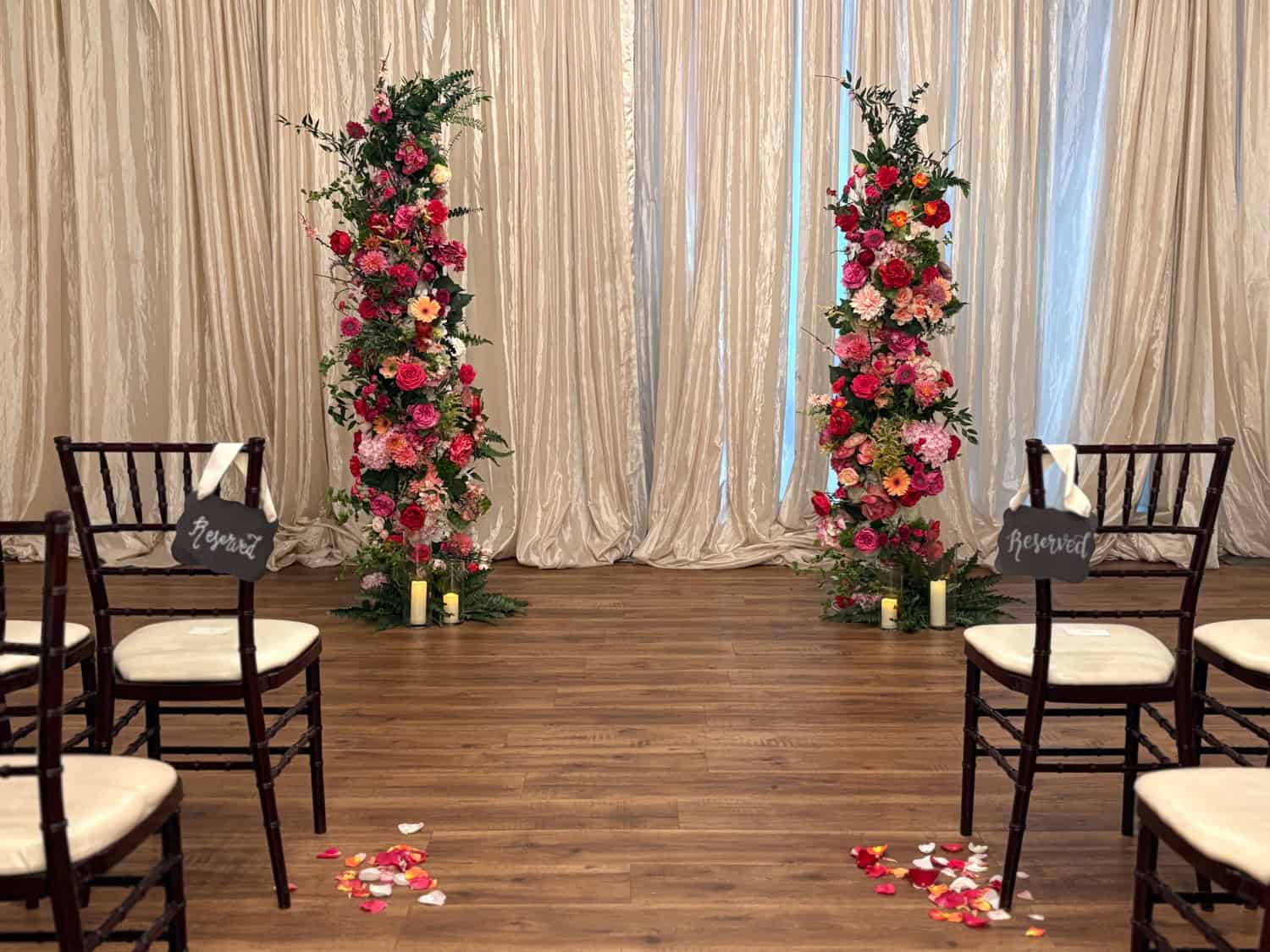 Wedding ceremony setup with floral arches and chairs on wooden floor.