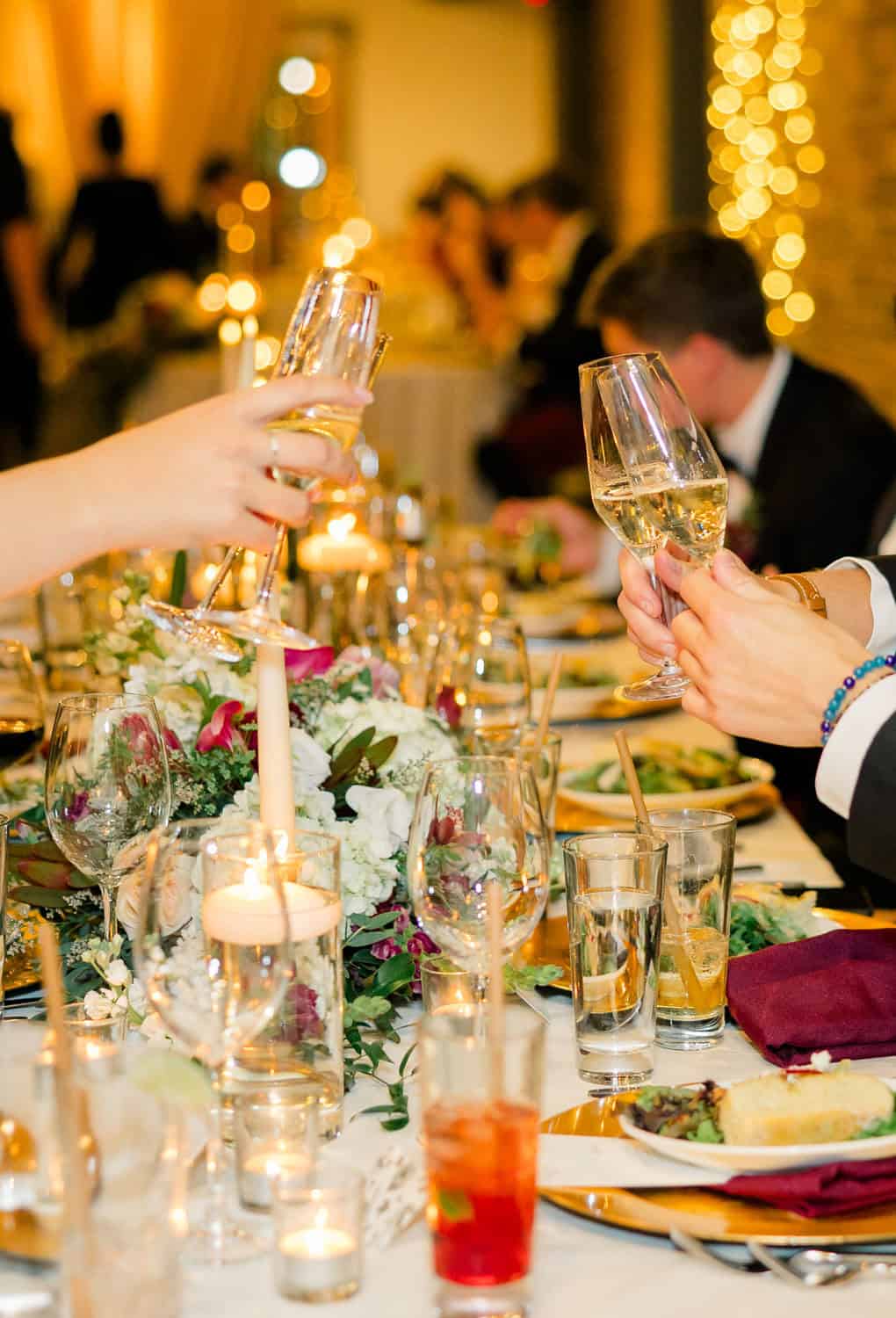 Guests clinking champagne glasses at a wedding reception with decorated table.
