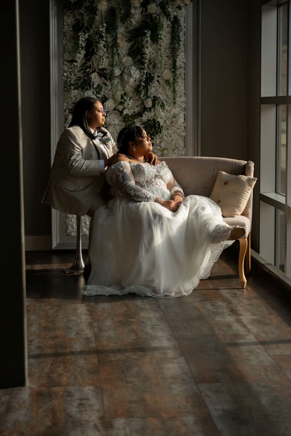 Bride and bridesmaid sitting by the window in wedding dresses.