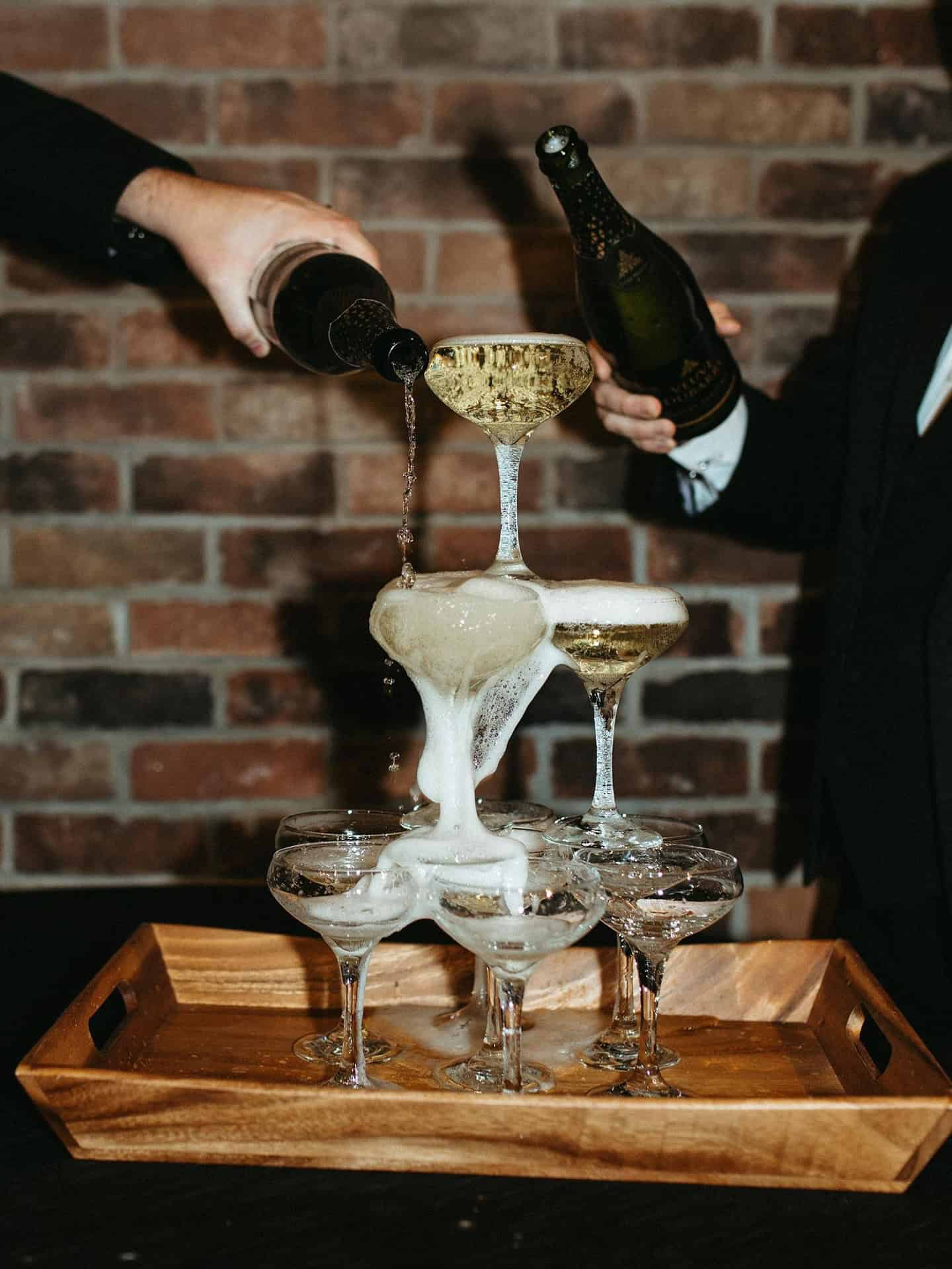 Champagne glasses stacked in a tower with two people pouring champagne.