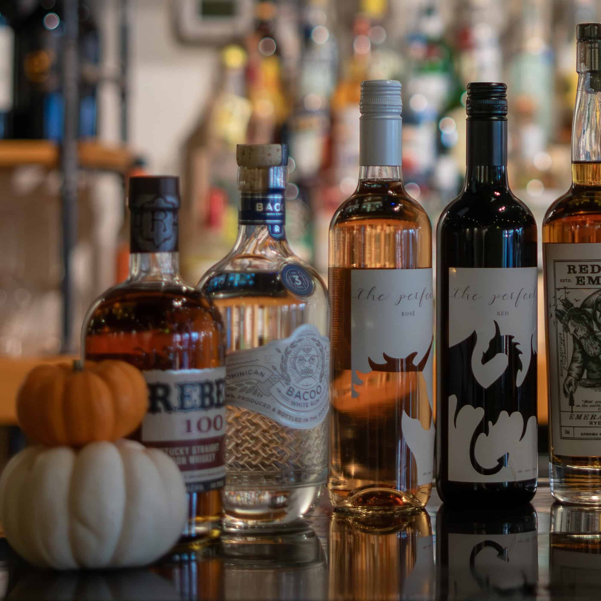 Variety of whiskey bottles with pumpkins on a bar counter.