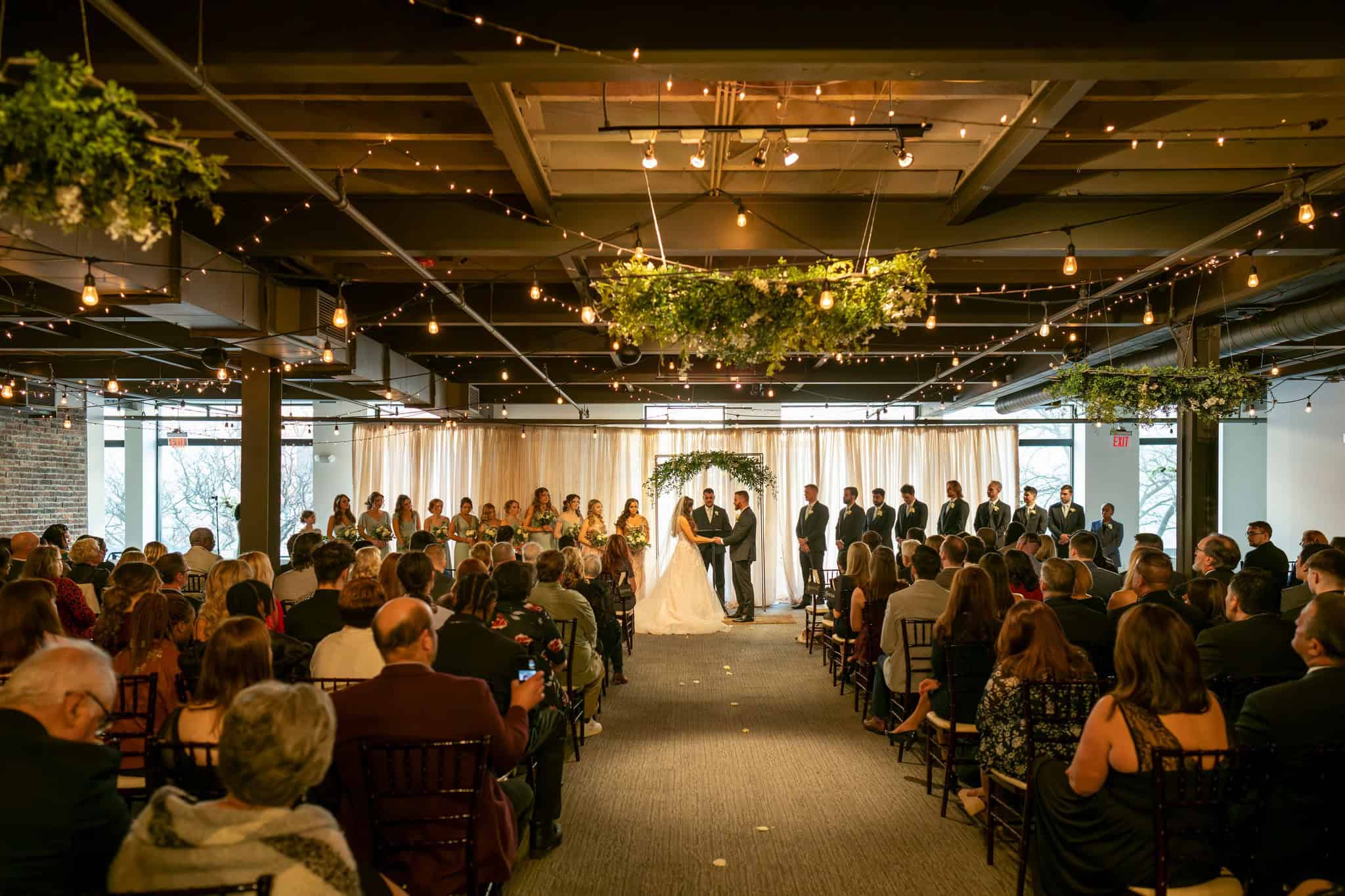 Wedding ceremony at SKY Armory with guests and couple under floral arch.