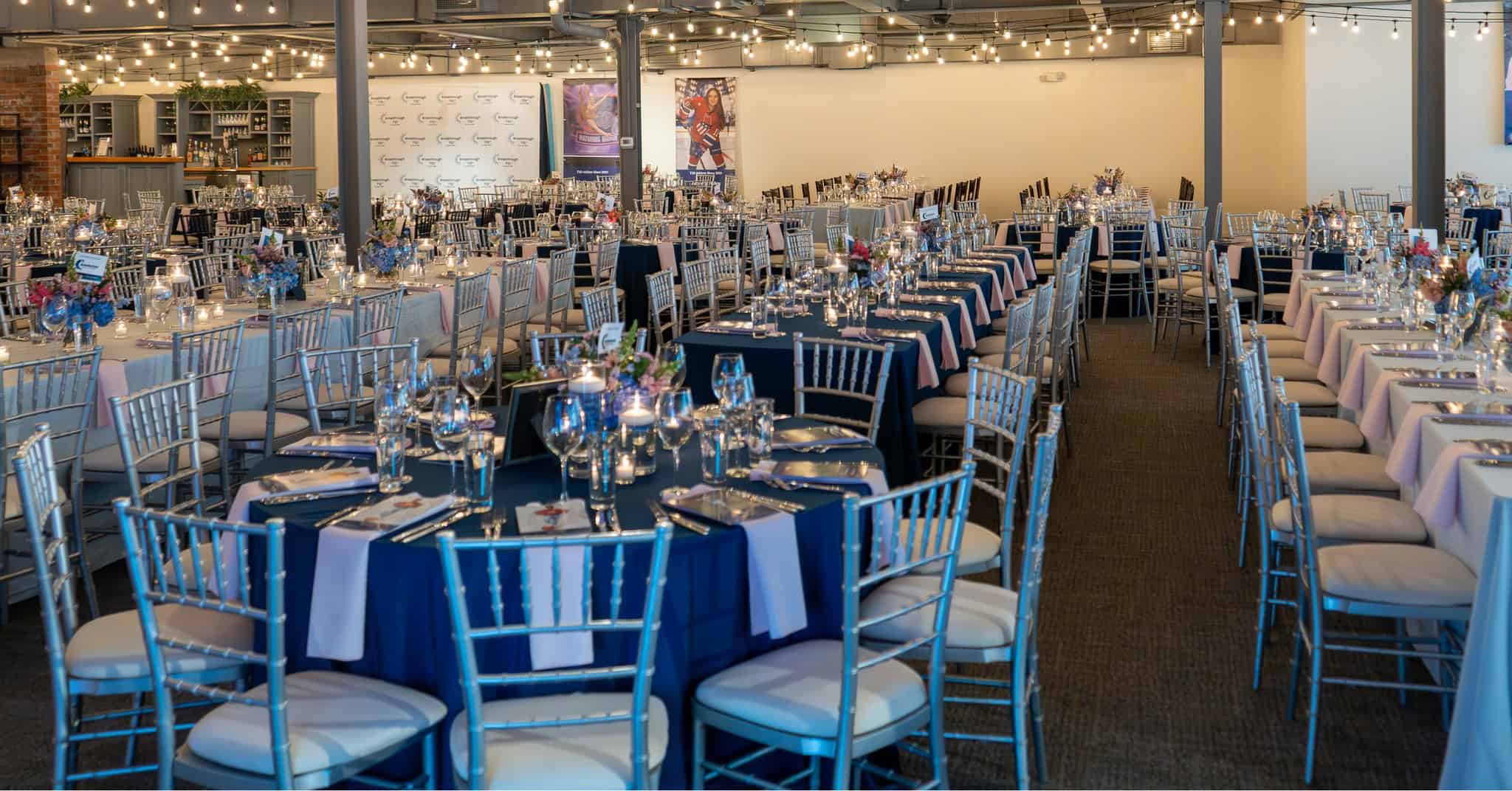 Event setup with round tables, blue tablecloths, and silver chairs at SKY Armory.