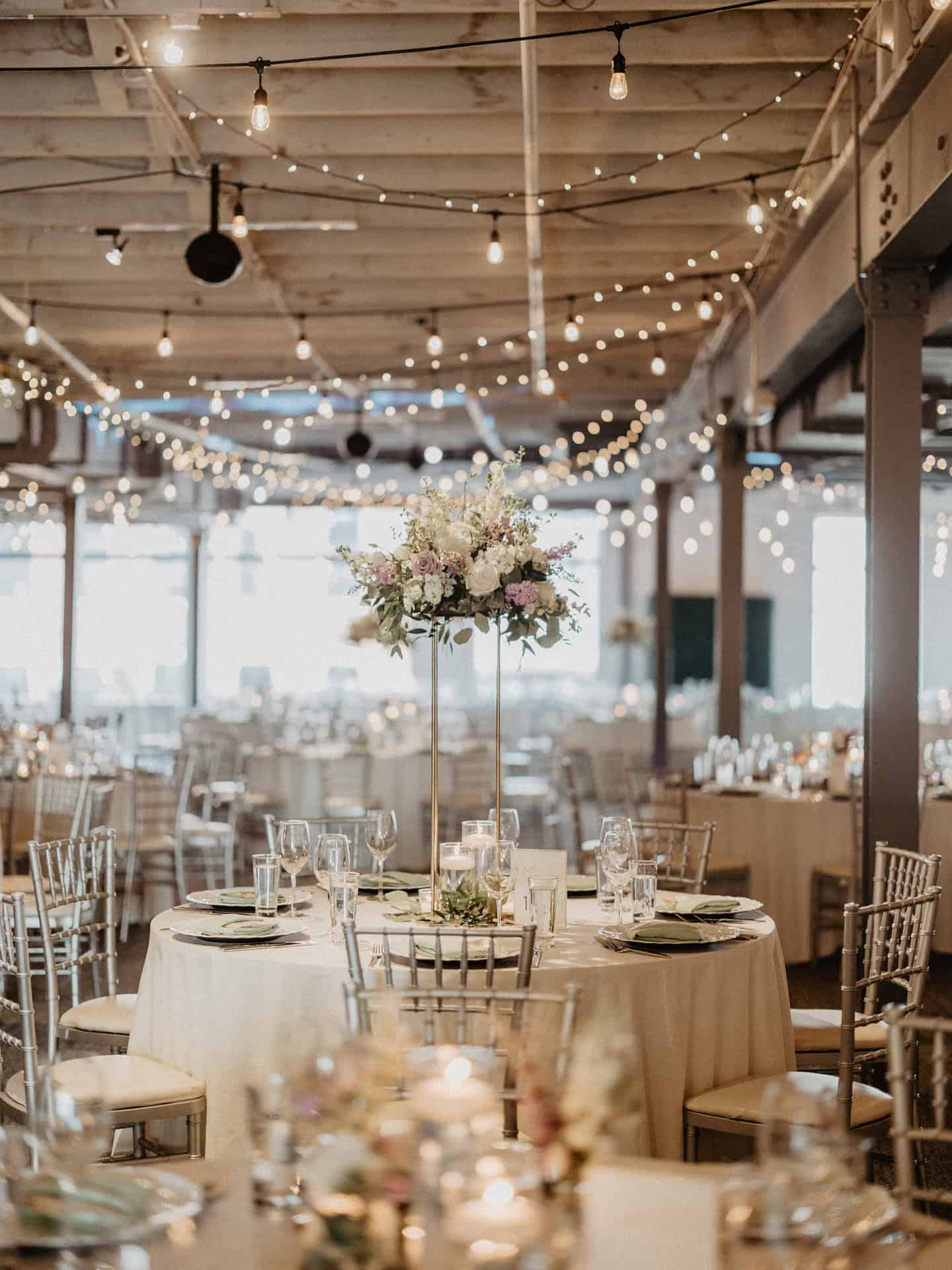 Beautiful banquet hall decorated with string lights and floral centerpieces for a wedding or event.