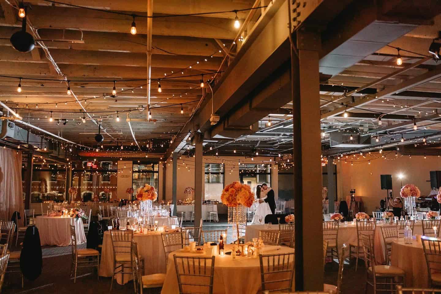 Indoor event space decorated with string lights and floral centerpieces.