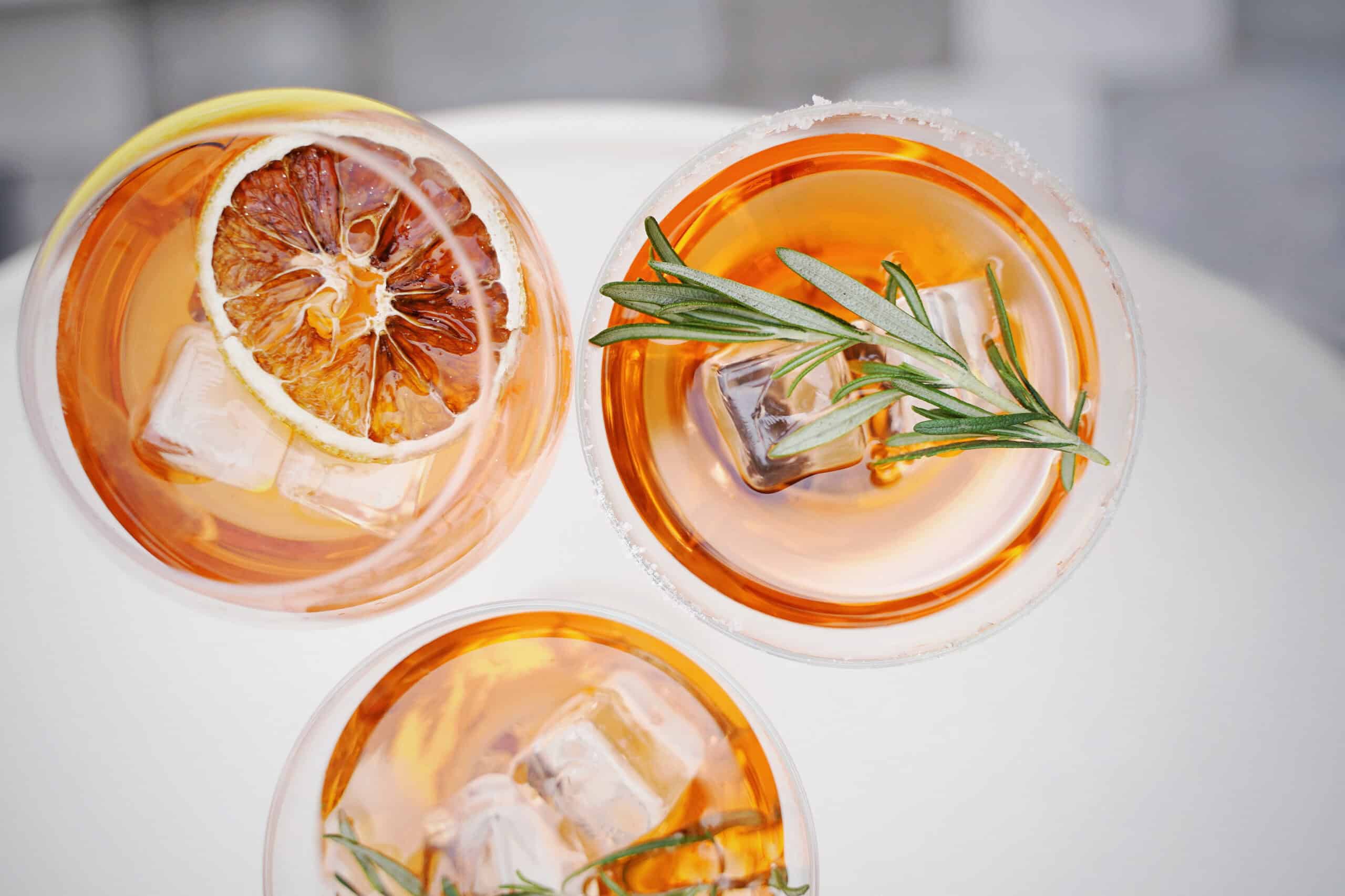 Three glasses of citrus cocktail with ice, lemon, and rosemary garnish.