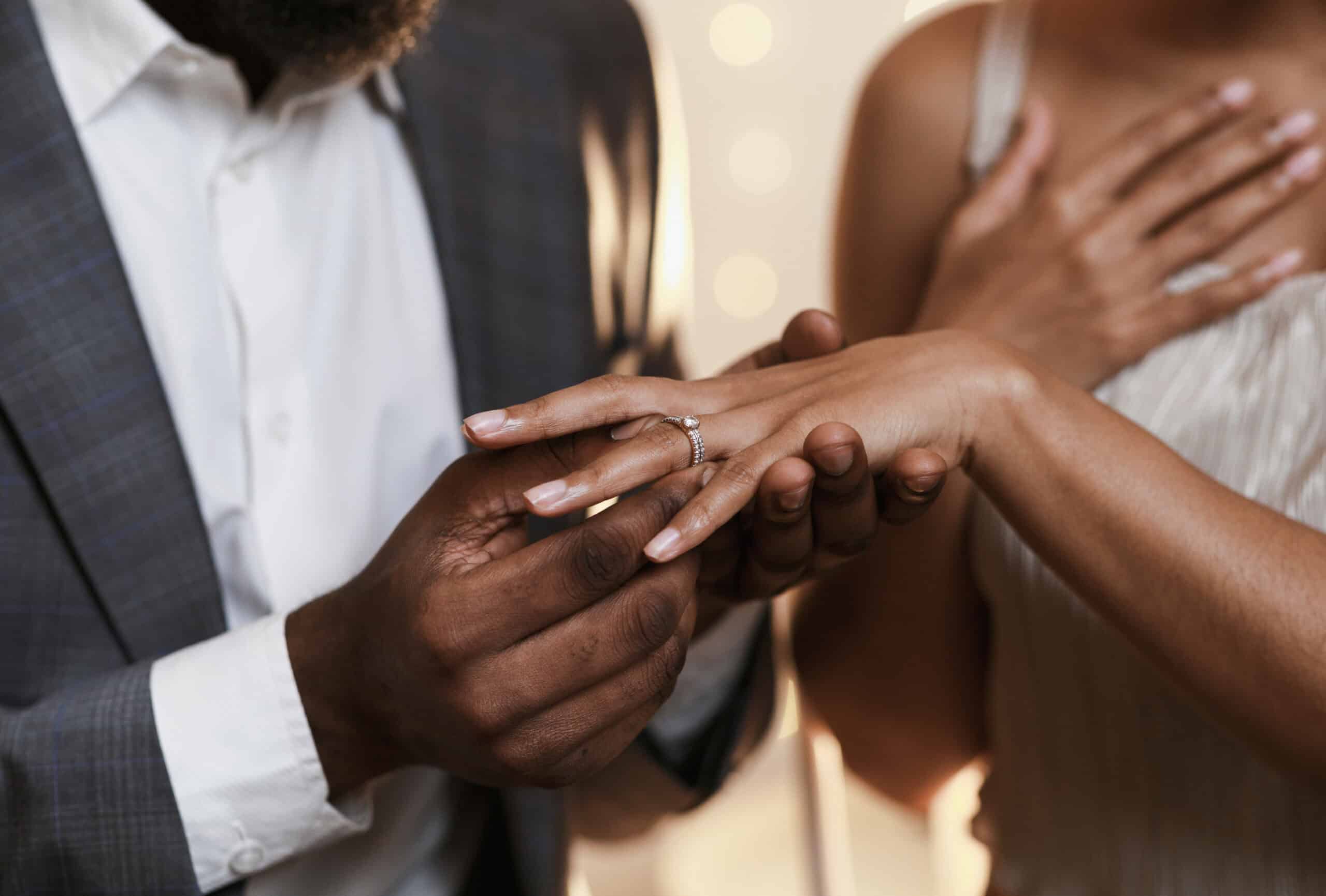 Couple exchanging rings during a marriage proposal in a romantic setting.