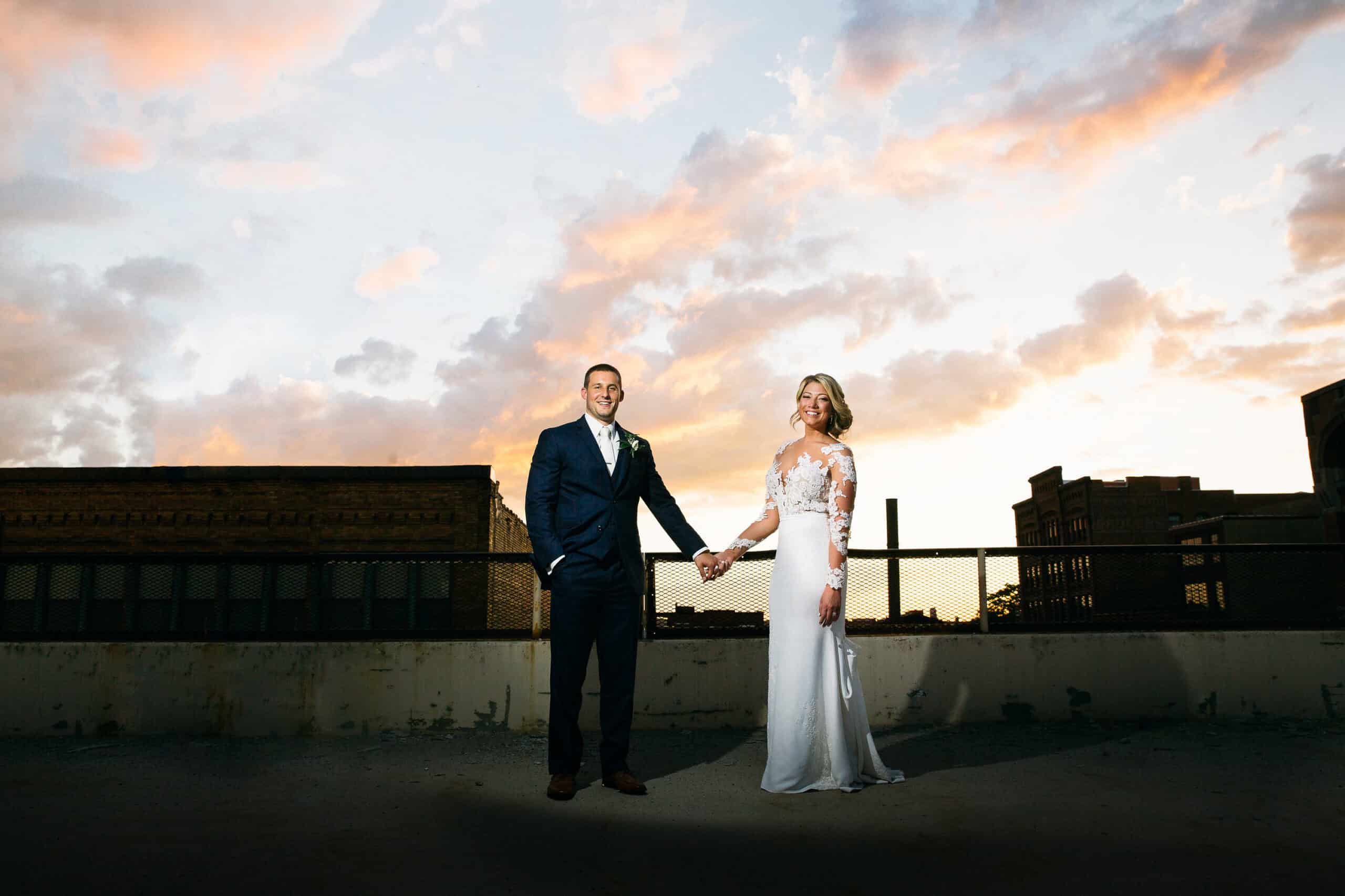 Bride and groom holding hands on rooftop during sunset for romantic wedding.