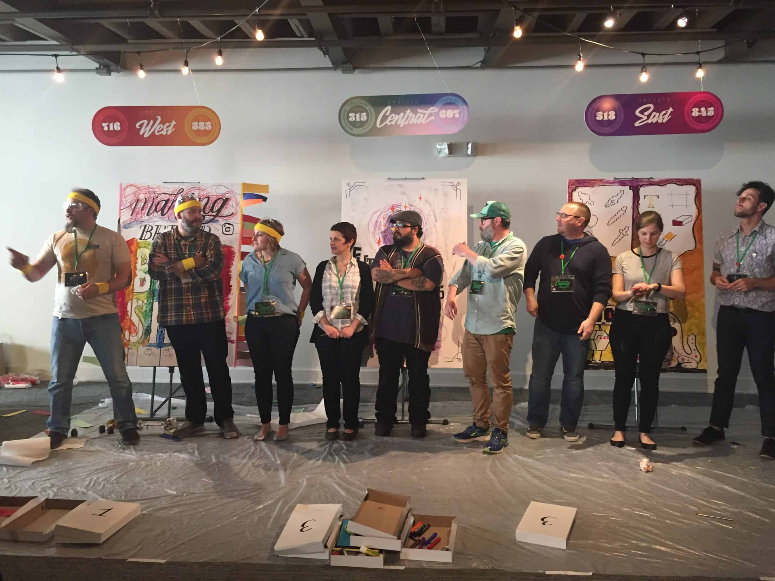 Group of people on stage at SKY Armory event with colorful signs overhead.