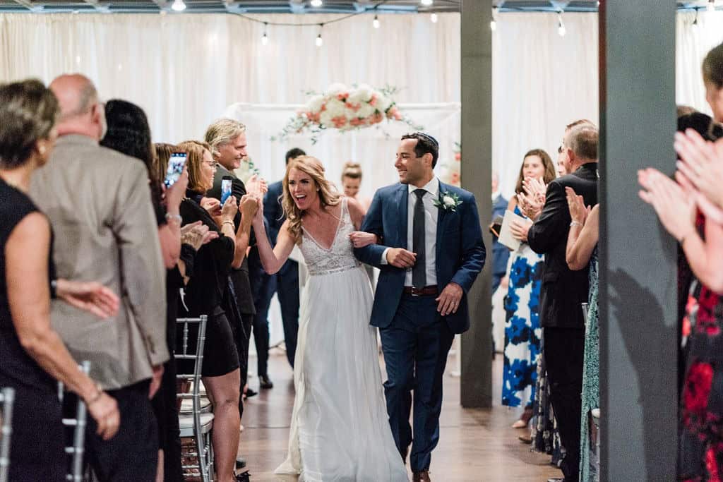 Bride and groom walking down the aisle with guests clapping.