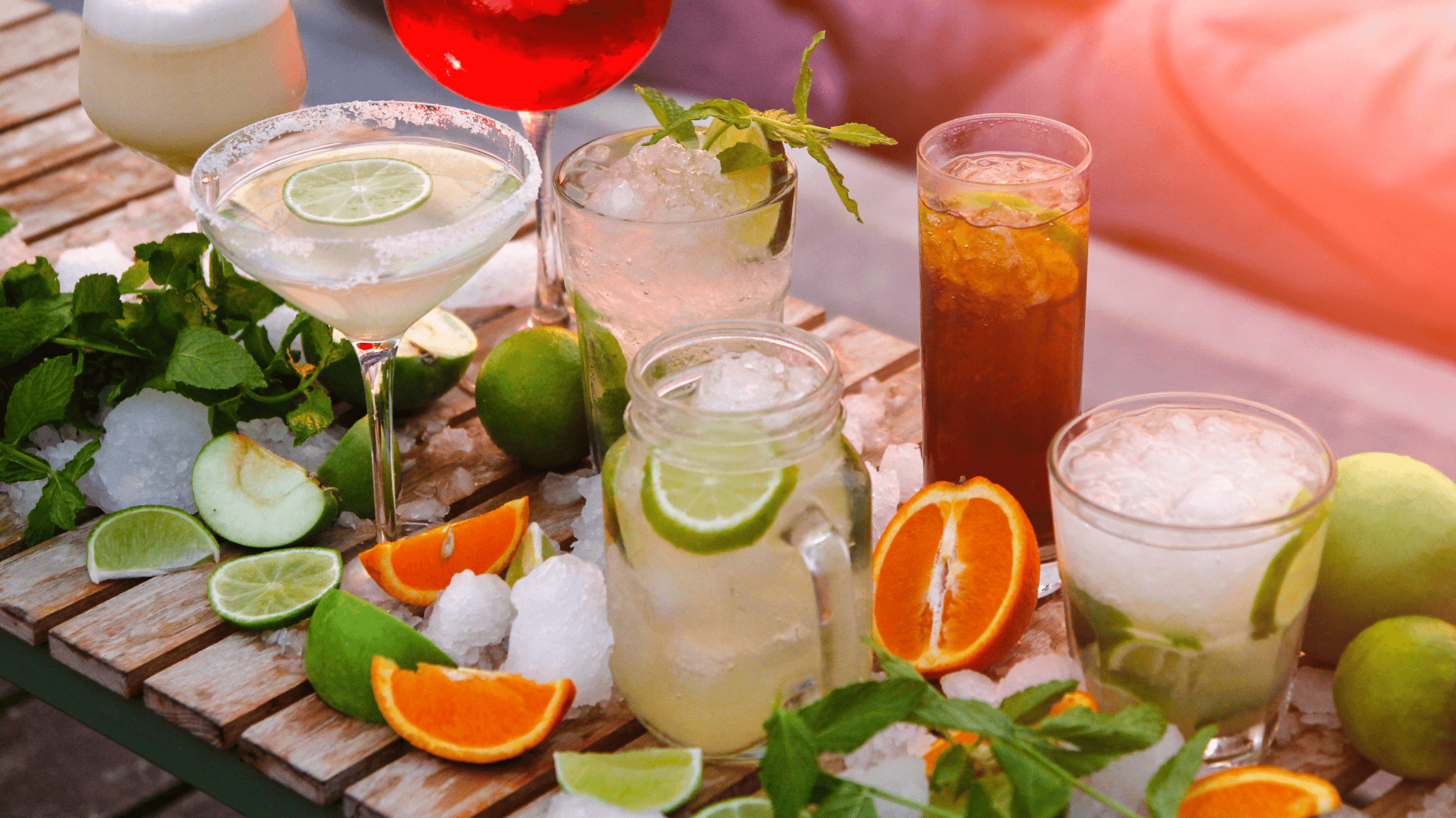 Assorted colorful cocktails with citrus fruits and ice on a wooden table.