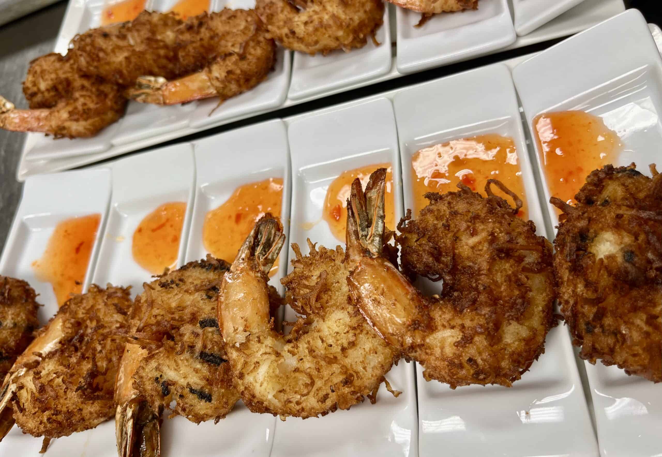 Crispy fried shrimp served with spicy orange dipping sauce on white plates.