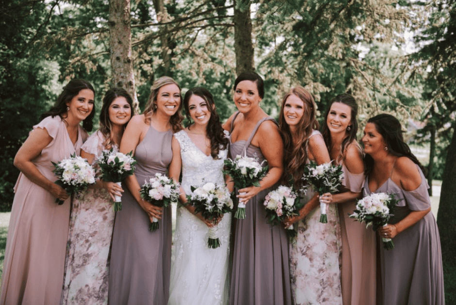 Group of bridesmaids in mismatched dresses holding bouquets at outdoor wedding.