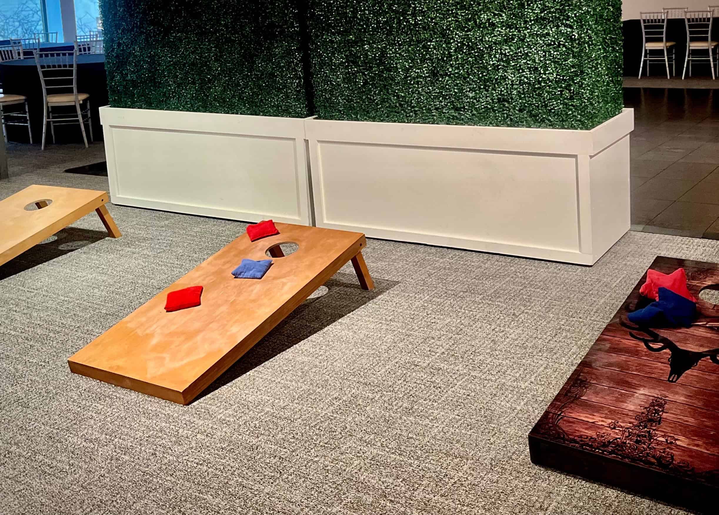 Indoor cornhole game with bean bags on wooden boards at a corporate event.