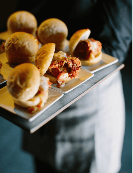 Mini meatball sliders with melted cheese on a serving tray.