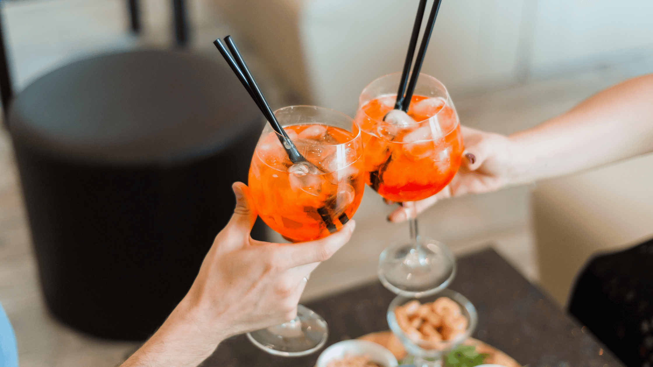 Two people clinking colorful cocktails in a cozy setting.