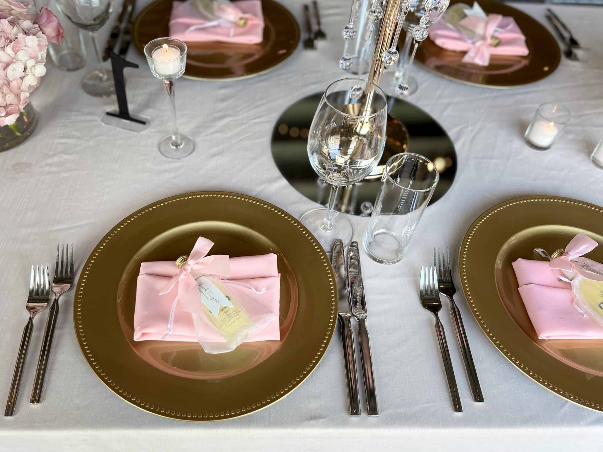 Wedding table with gold plates, pink napkins, and wedding favors.