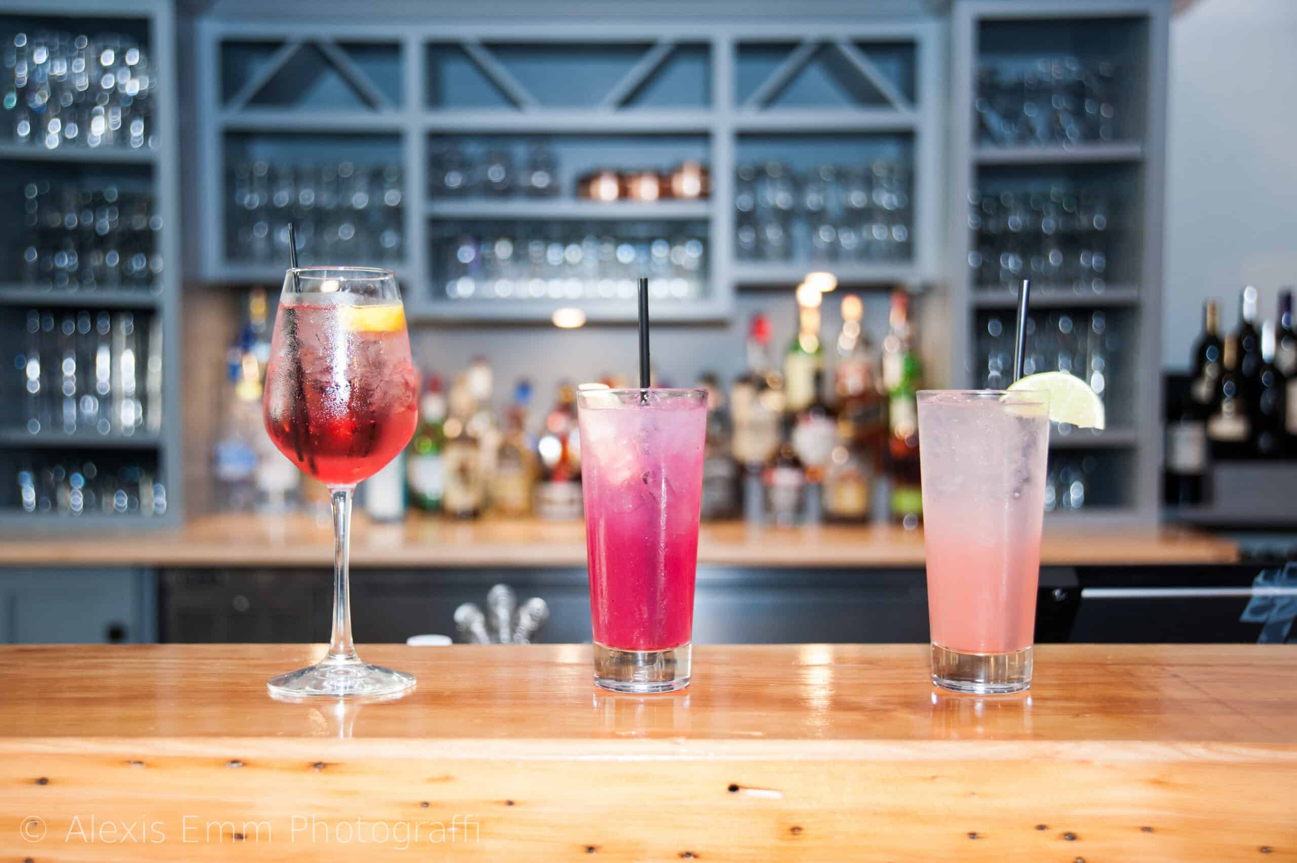 Three colorful cocktails on a bar counter with a blurred bar background.