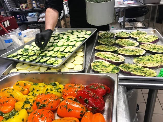 Colorful vegetable dishes including zucchini, eggplant, and peppers at farmers market.