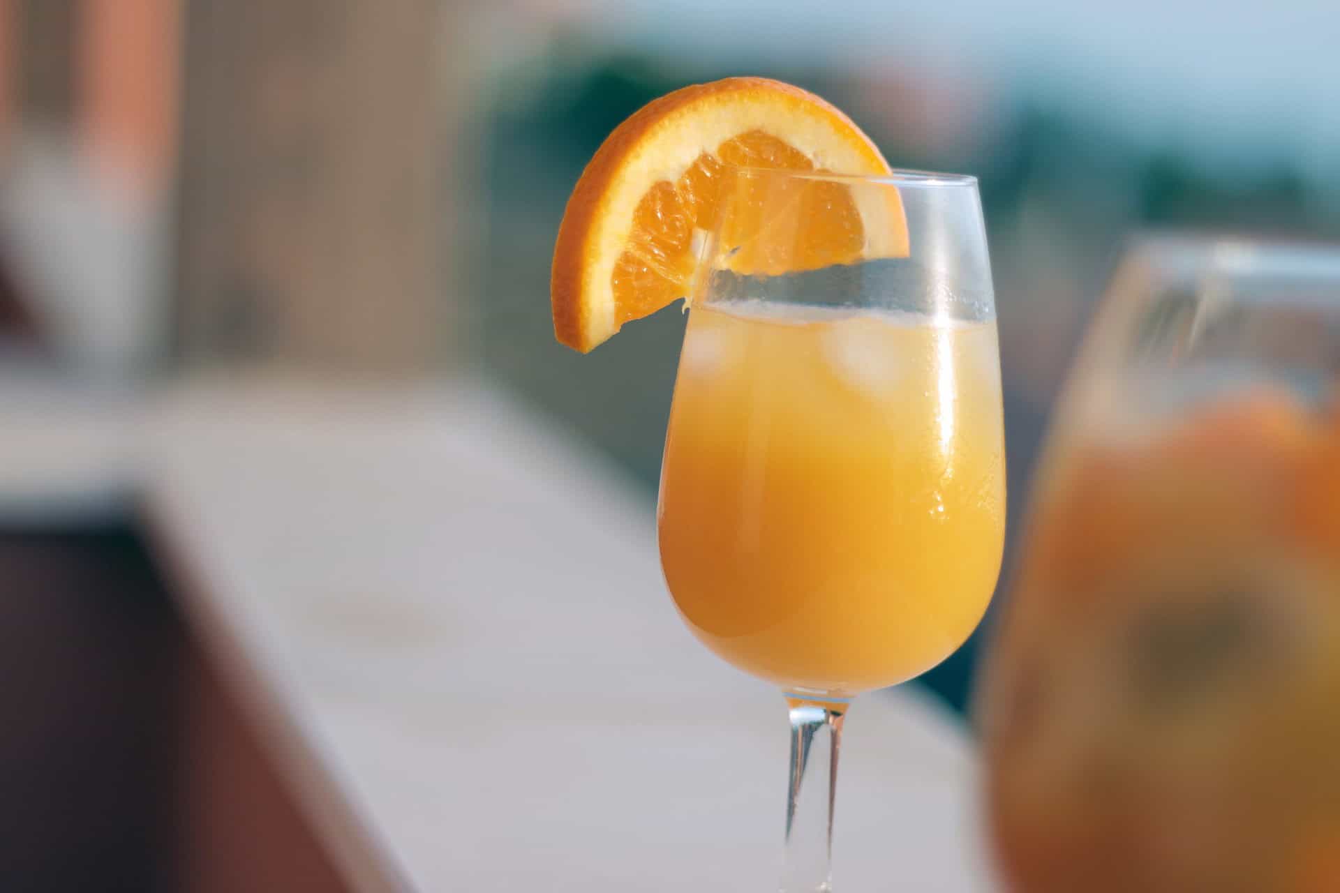 Orange cocktail with a slice of orange on a sunny outdoor table.