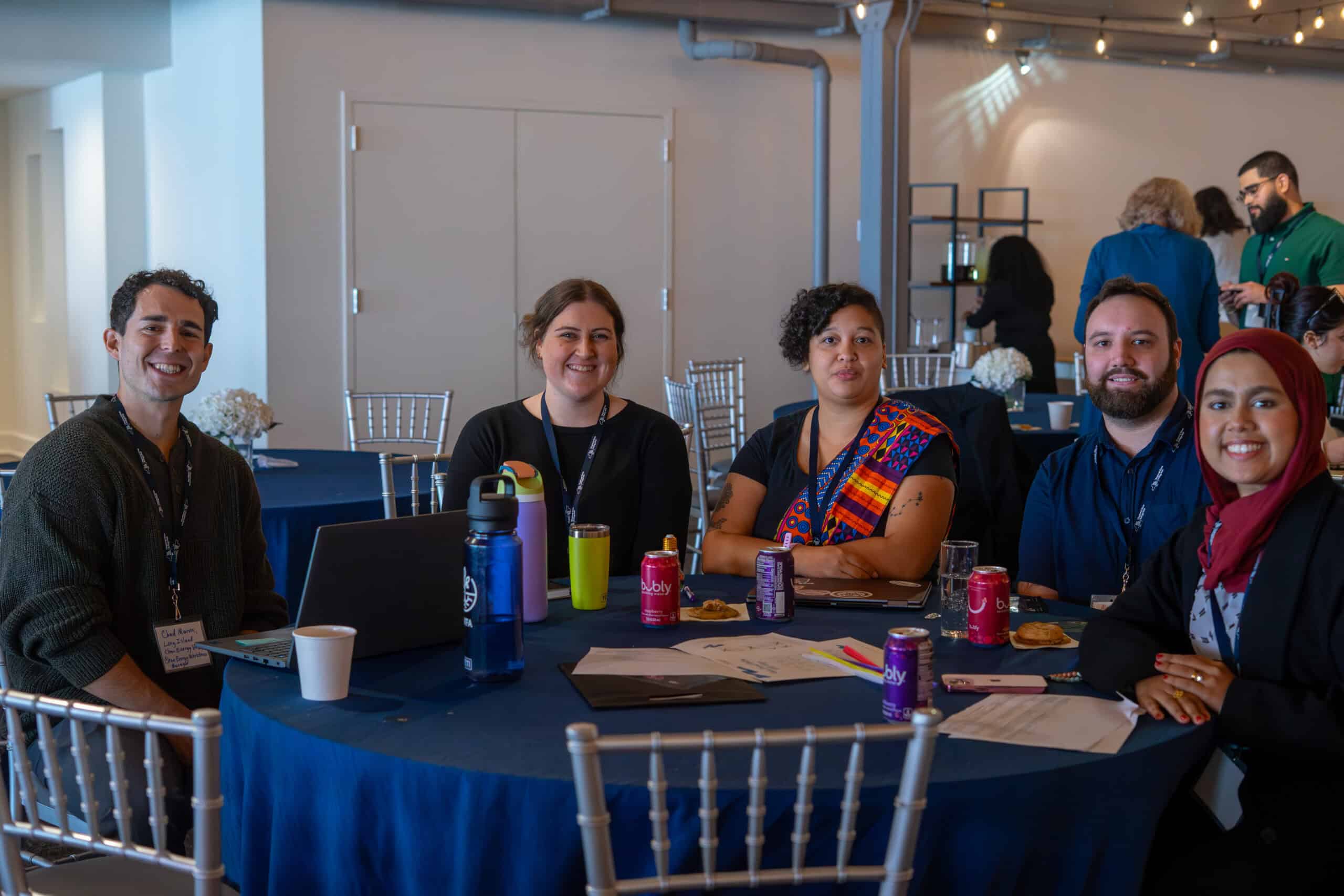 Diverse group of professionals at a corporate event table with drinks and laptops.