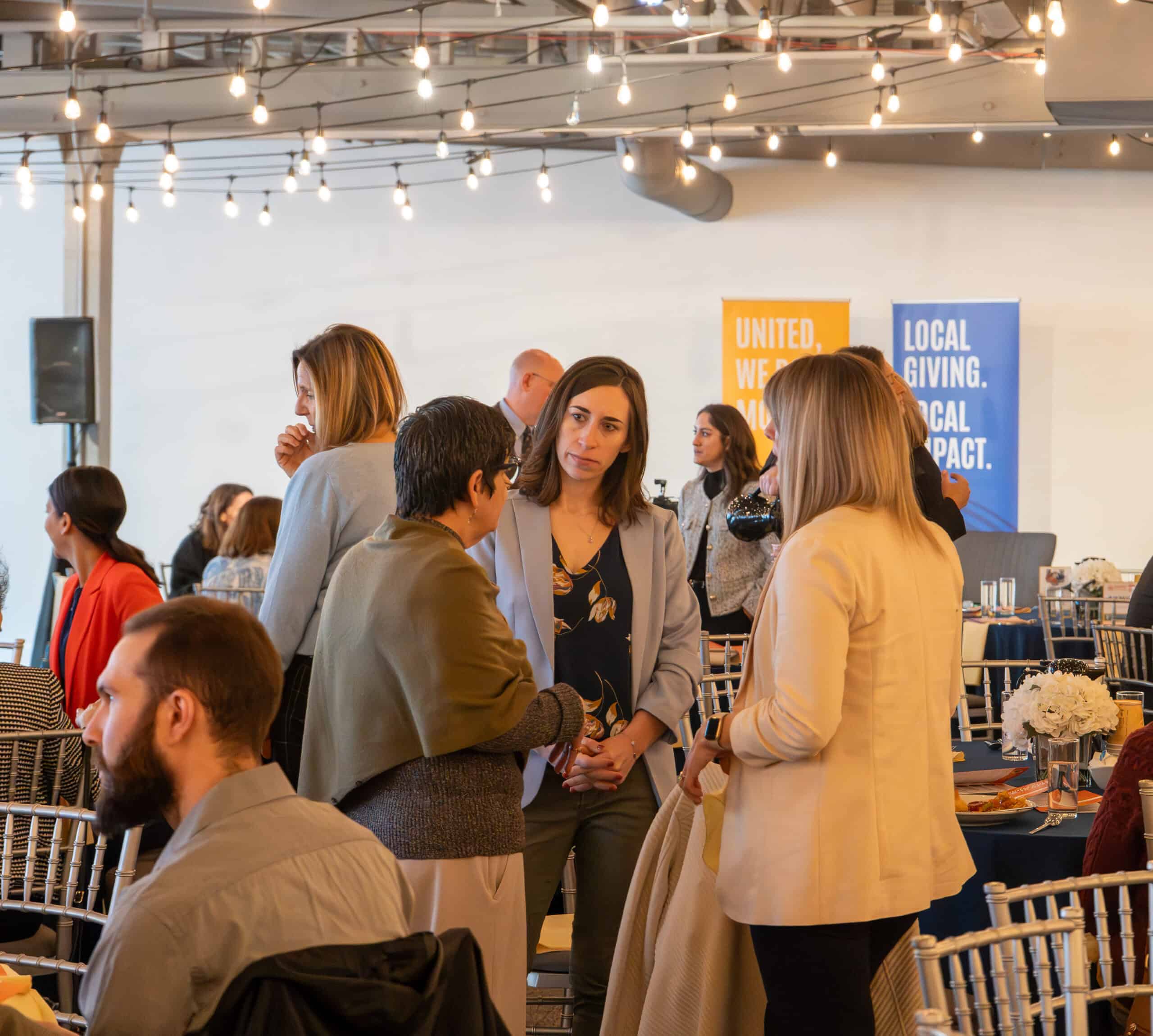 Business professionals networking at SKY Armory event with string lights overhead.
