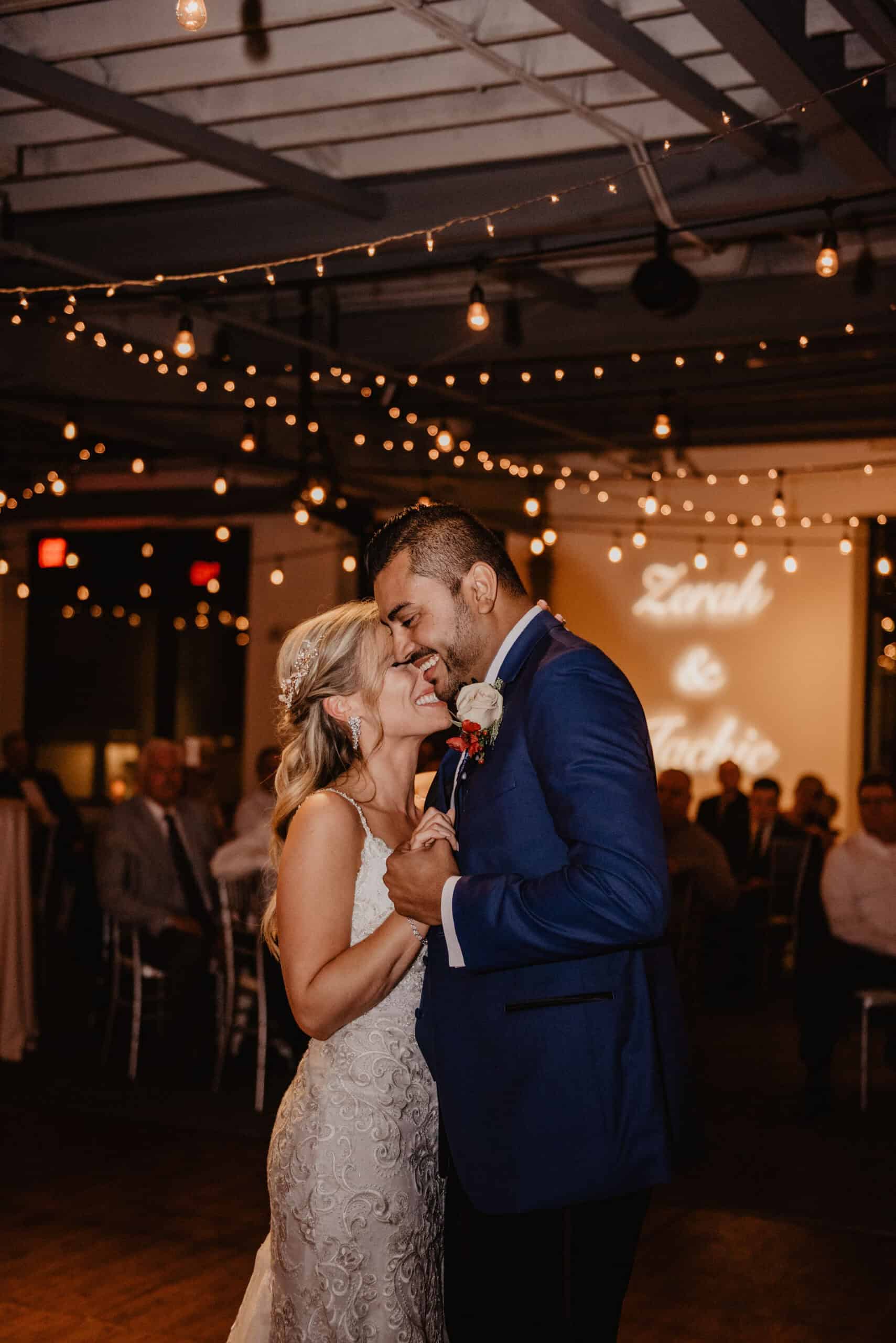 Happy wedding couple dancing at reception with string lights overhead.