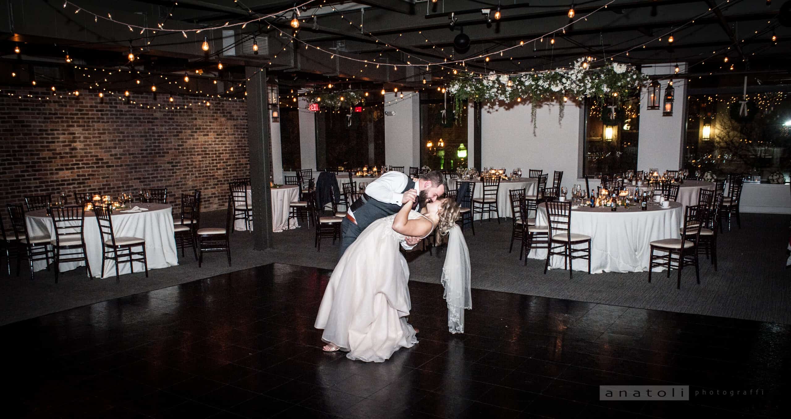 Bride and groom dancing at wedding reception with string lights overhead.