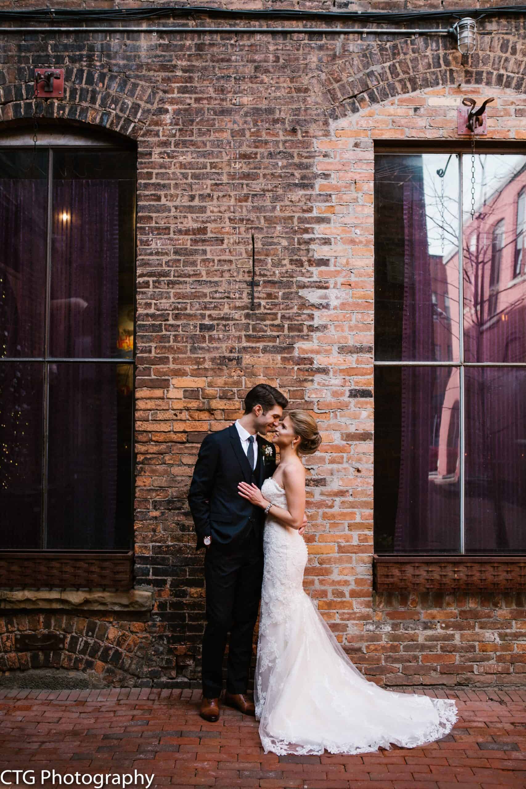 Bride and groom sharing a romantic moment against a brick wall.