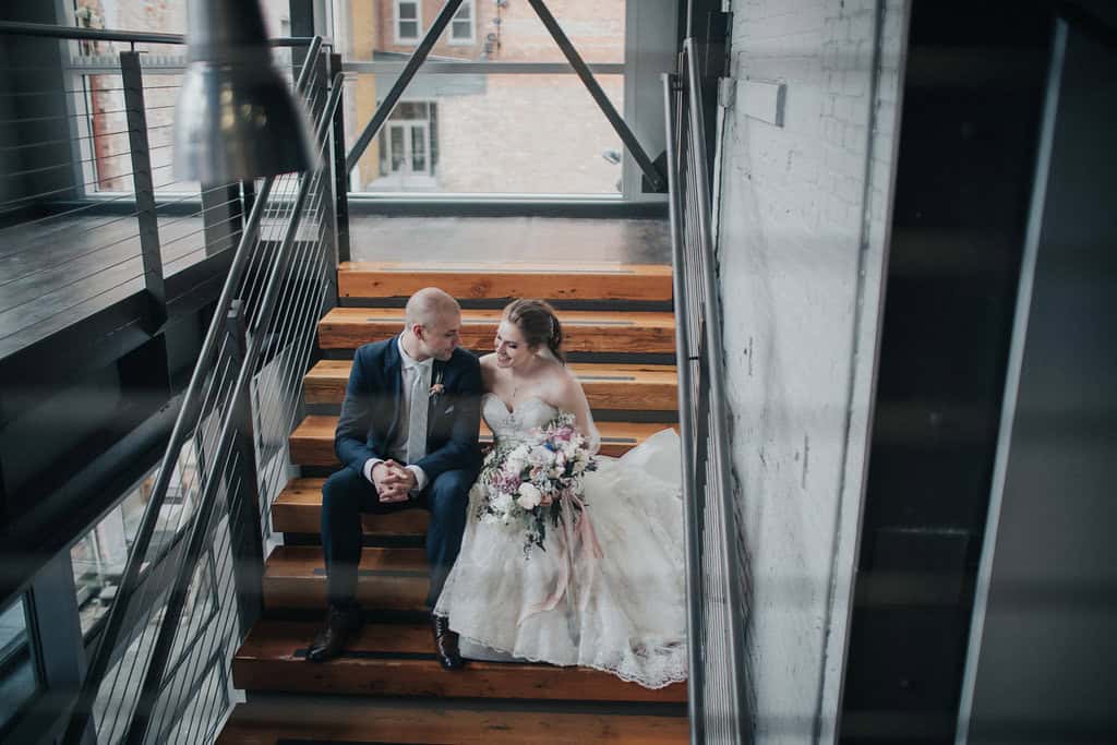 Bride and groom sitting on staircase during wedding celebration.