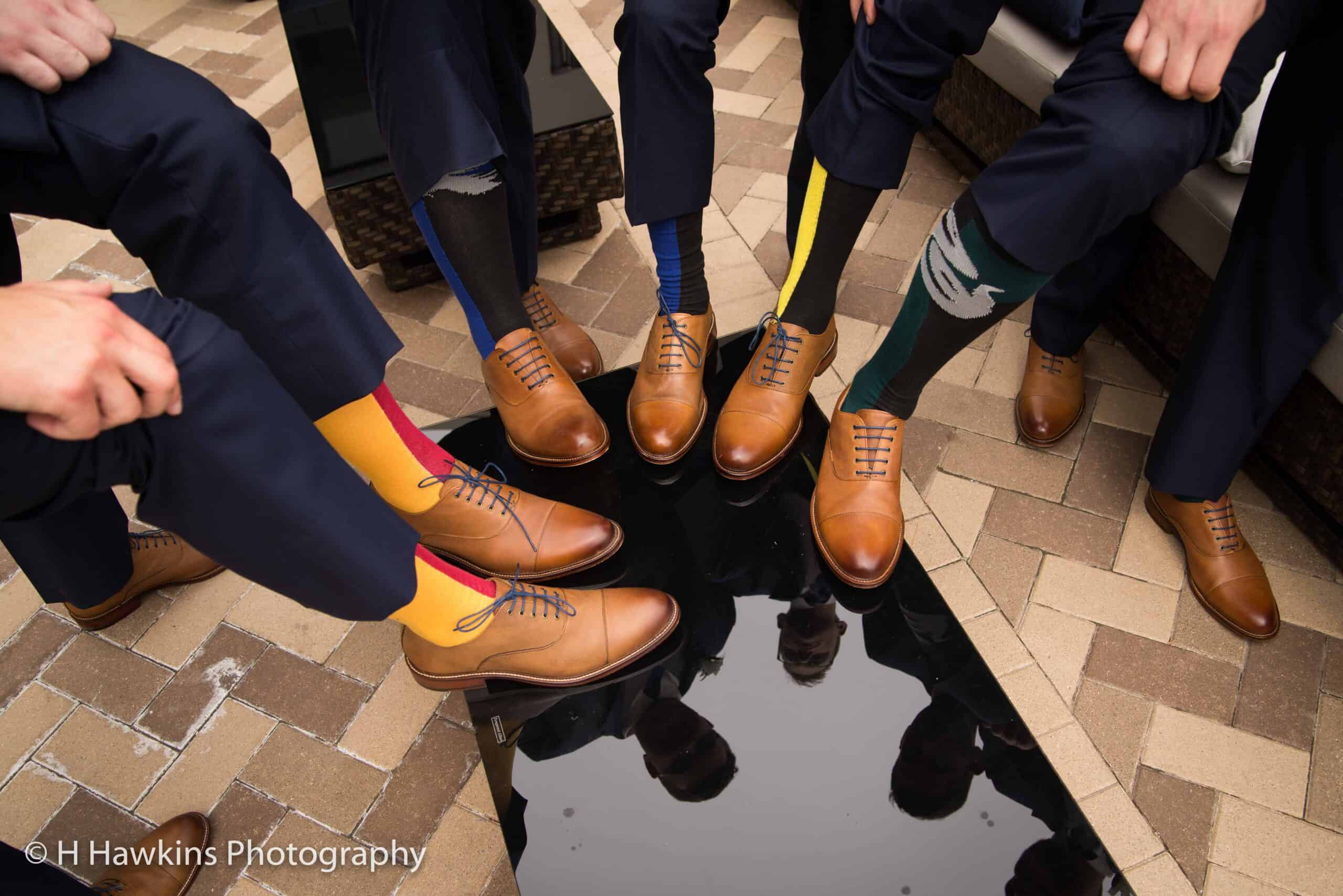 Group of men wearing colorful socks and brown dress shoes in a circle.