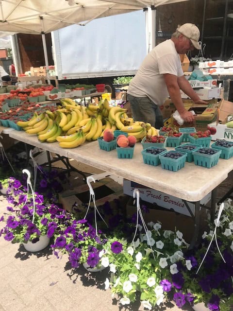 Vendor arranging fresh bananas and berries at farmers market stall.