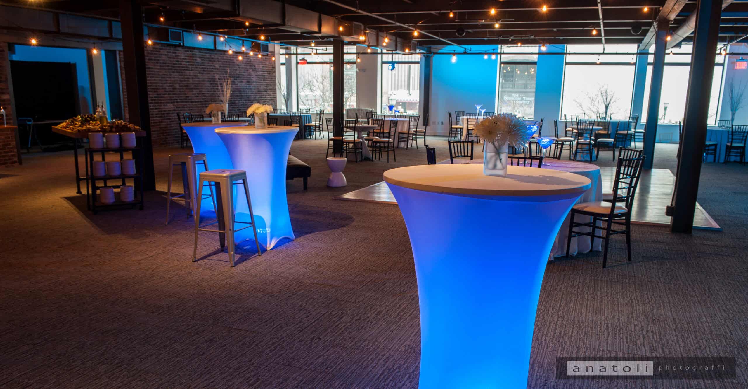 Modern event space with illuminated high-top tables and large windows.