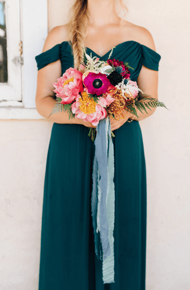 Woman holding a colorful bouquet of flowers in an off-shoulder dress.