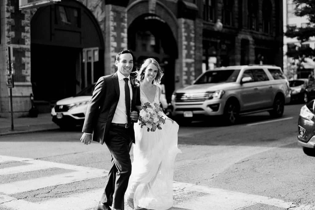 Happy wedding couple crossing the street in city setting.