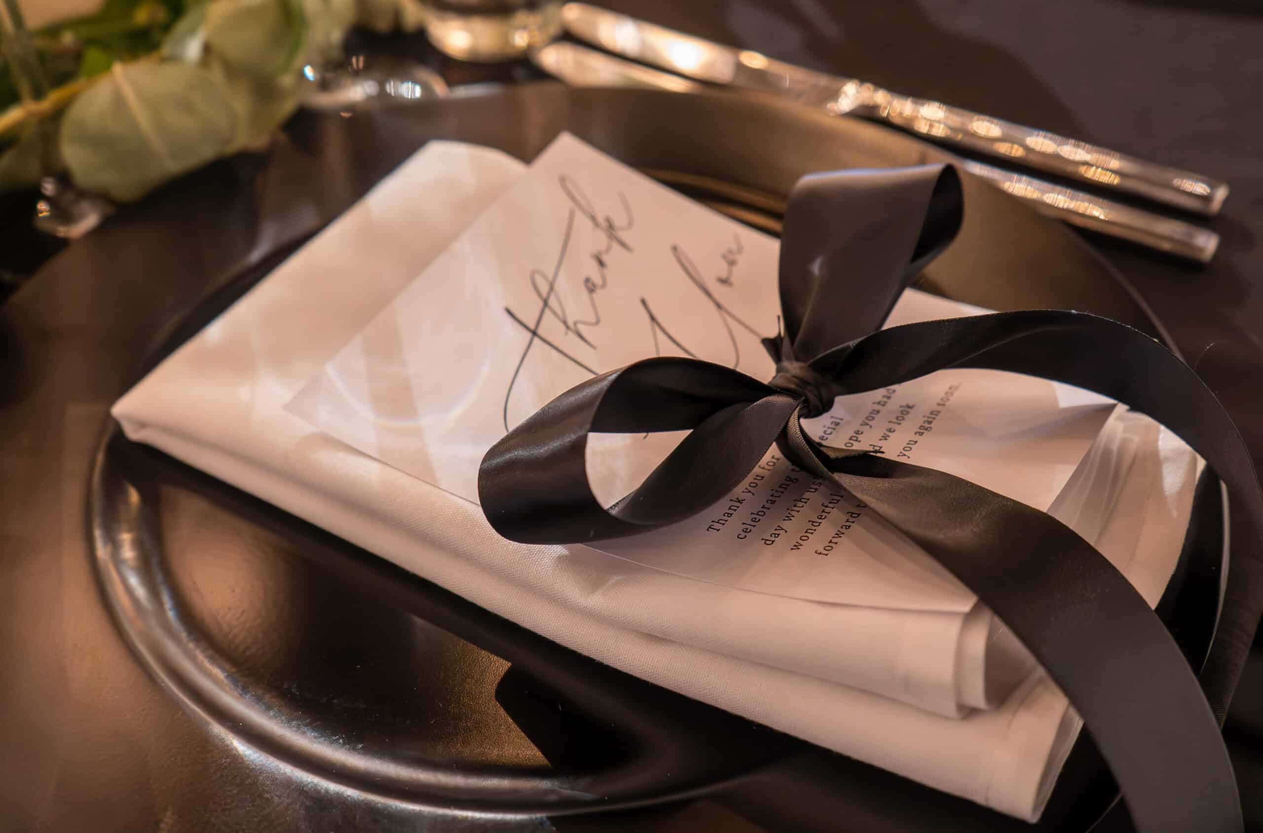 Rolled white napkin tied with black ribbon on a silver tray.