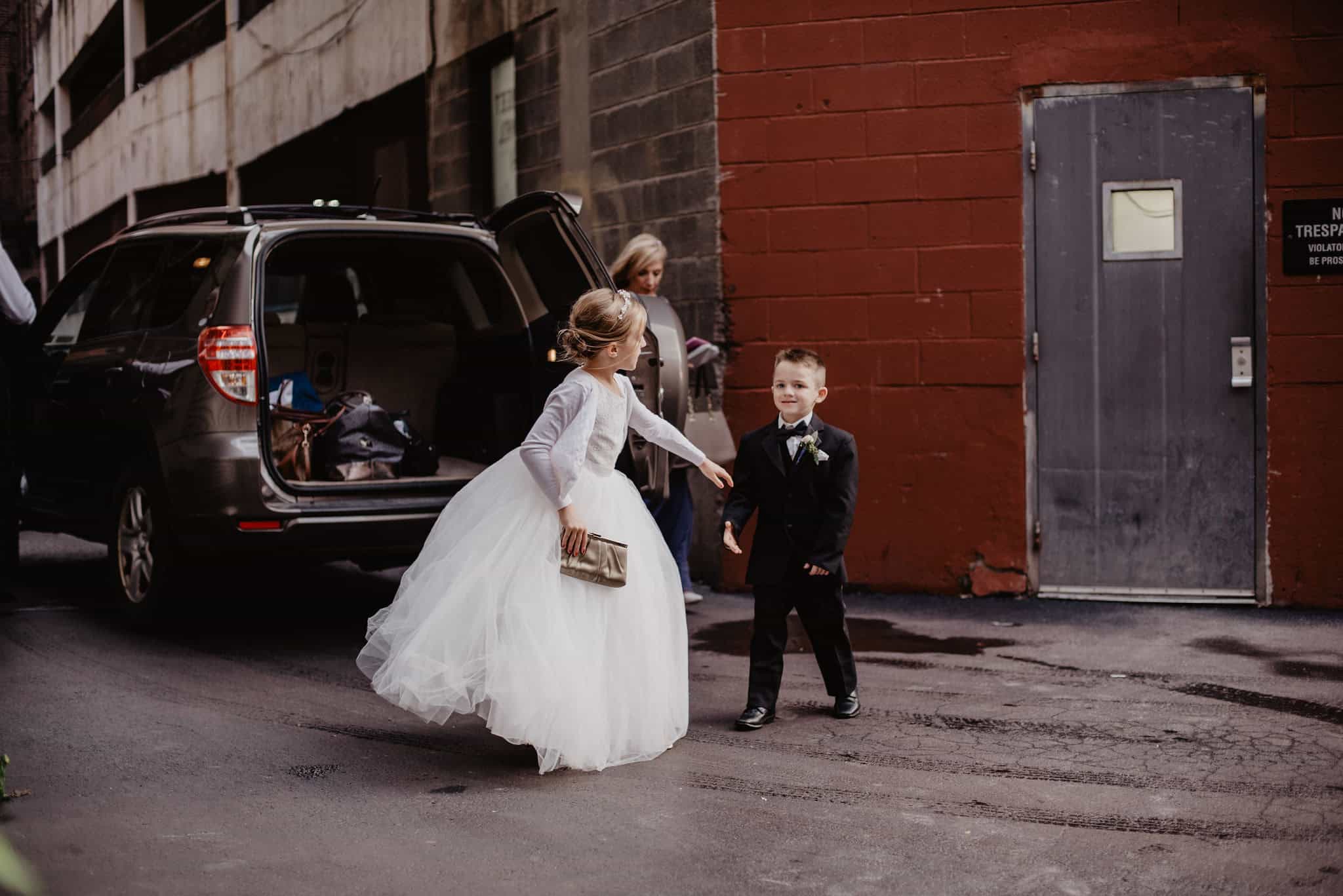 Children in formal wear standing outside near a black vehicle.