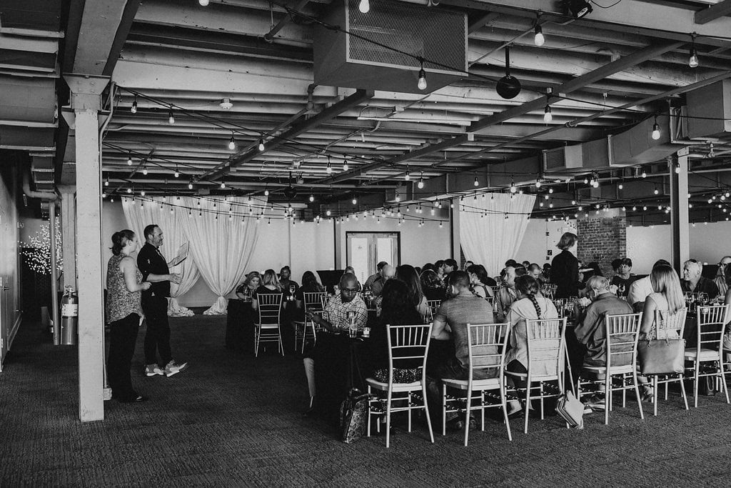 Indoor event space with guests seated at tables and string lights overhead.