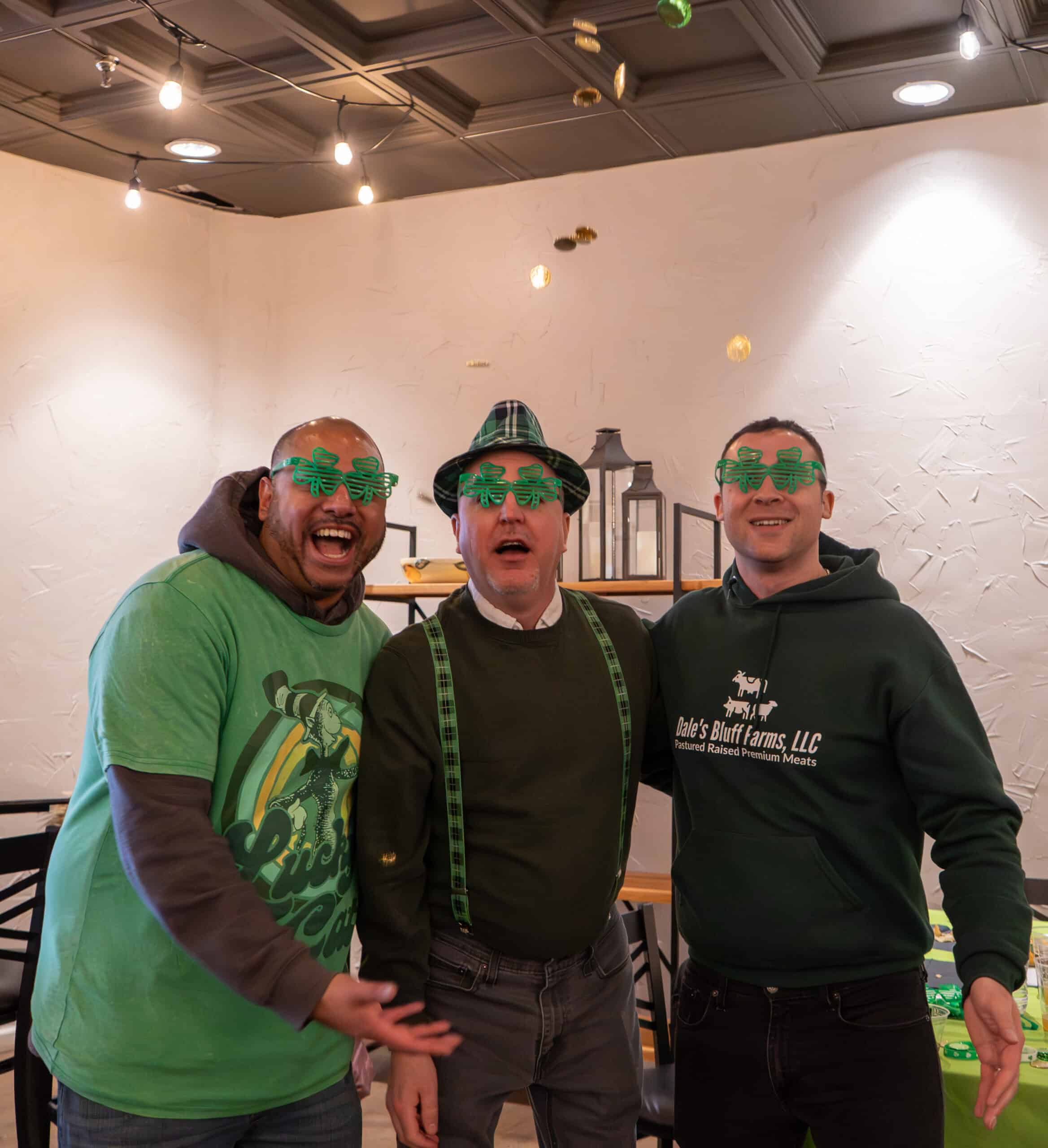 Three men celebrating St. Patrick's Day at Sky Armory with green glasses and festive attire.